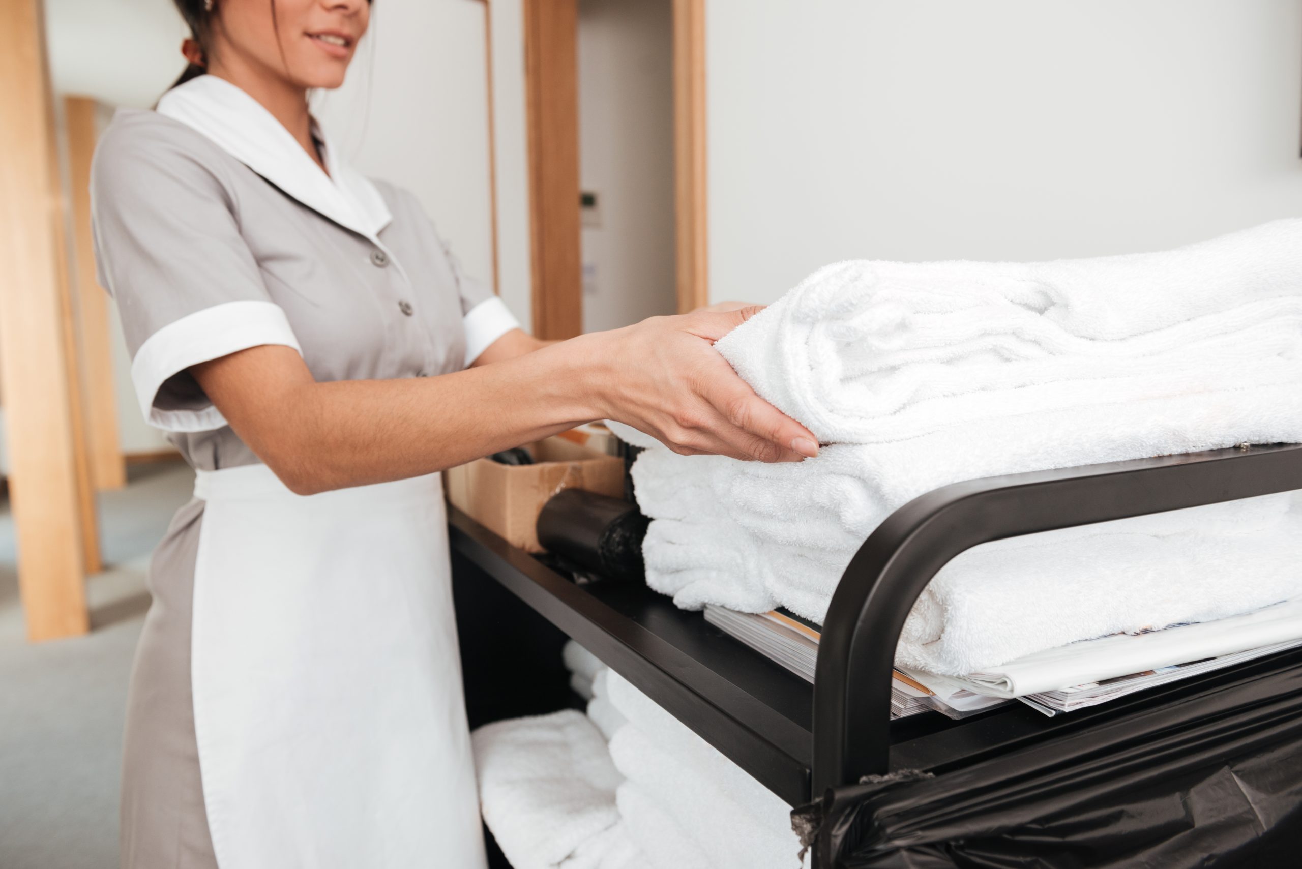 Cropped image of a smiling young maid taking fresh towels from a housekeeping cart